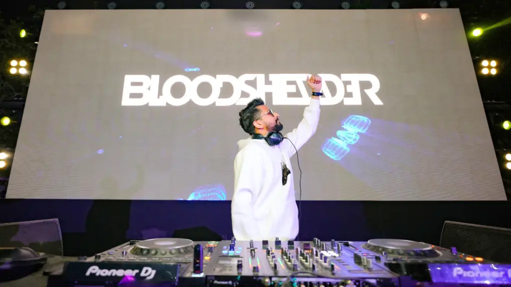 DJ Bloodshedder performing live on stage with a branded LED backdrop